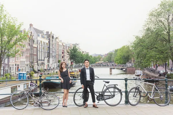 戶外拍攝妝容：自然淡妝配長直髮，女士身穿黑色連身裙，與男伴在運河橋上合照
